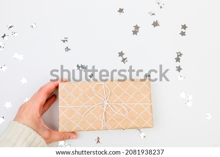 gifts or presents boxes silver confetti on white table top view. female hands in a warm sweater are holding a gift
