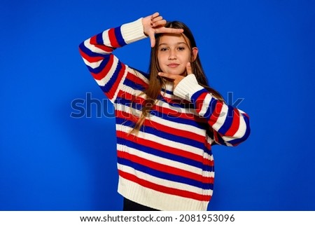 Adolescent girl in a striped sweater making the gesture of being framed by a camera. She practices to be an actress when she's older