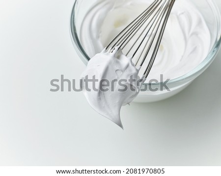 glass bowl of whipped egg whites cream on white kitchen table background, top view Royalty-Free Stock Photo #2081970805