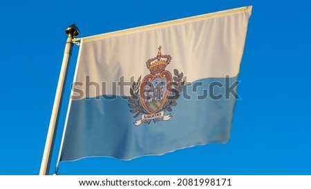 National flag of San Marino on a flagpole in front of blue sky with sun rays and lens flare. Diplomacy concept. International relations. Space for text.