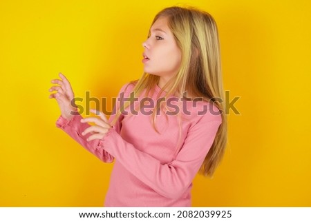 Displeased caucasian little kid girl wearing long sleeve shirt over yellow background keeps hands towards empty space and asks not come closer sees something unpleasant