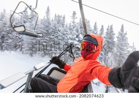 Ski vacation - skier in ski lift taking selfie photo or video using mobile phone. Ski winter vacation concept. Skiing on snow slopes in mountains, Woman having fun on snowy day. Winter sport activity. Royalty-Free Stock Photo #2082074623