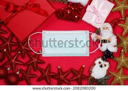 Protective surgical mask with christmas decorations over red background. Christmas concept background. Celebration in self-isolation, coronavirus, covid-19. Copy space. Space for text.