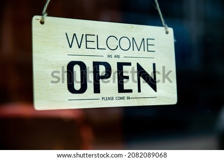 Welcome we are open signage hanging on the front of shop and restaurant, wooden welcome open sign on the blurred background.