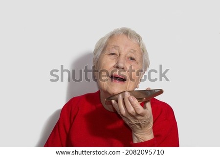 Charming elderly woman using voice recognition function on cell phone. Modern senior female holding electronic gadget, sending vocal message or online messenger
