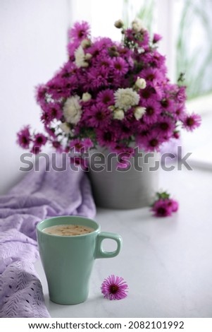 Cup of aromatic coffee, beautiful flowers and violet cloth on white table