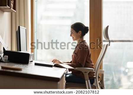 Happy successful millennial indian ethnic business lady working in modern home office, using computer software applications, creating new internet project, communicating distantly with client. Royalty-Free Stock Photo #2082107812