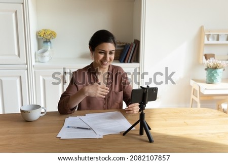 Smiling beautiful young indian woman recording educational video on cellphone web camera, sharing knowledge online, streaming educational webinar in social network, professional videoblogging concept. Royalty-Free Stock Photo #2082107857