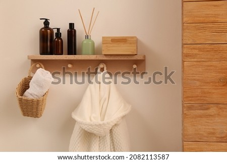 Wooden shelf with toiletries, fresh towel and bathrobe on beige wall. Interior element Royalty-Free Stock Photo #2082113587