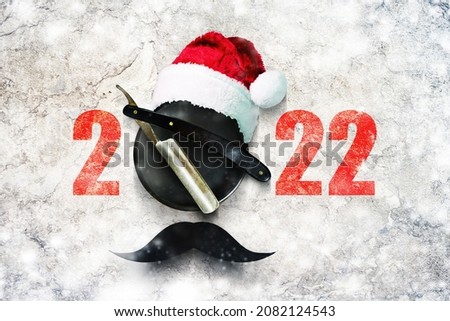 Razor on a plate for foam with a Santa Claus hat on a gray background. Numbers 2022. Greeting card Happy New Year and Merry Christmas for a hairdresser and barbershop. Snow effect