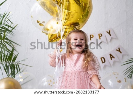 happy little blond girl in pink dress holding balloons and celebrating her birthday