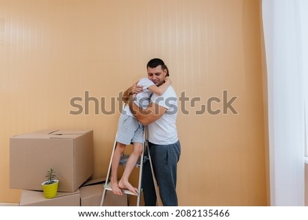 A young man and his son are standing in a new apartment after moving against the background of cardboard boxes and enjoying the housewarming. Housewarming, delivery and transportation of goods, purcha