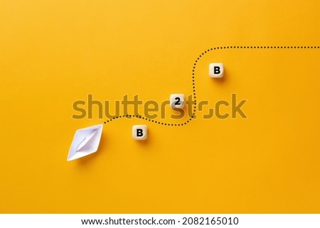 Origami paper boat passes through the wooden cube barriers with the acronym B2B. Business to business concept. Royalty-Free Stock Photo #2082165010