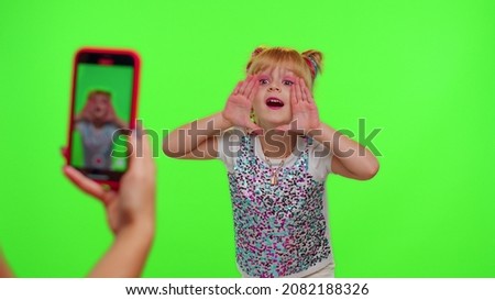 Lovely little Caucasian kid girl blogger front of phone camera record video enjoy dance content on green chroma key background. Social distance coronavirus pandemic concept. Freedom active lifestyle