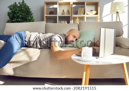 Man lying on sofa at home. Sad bored lazy passive guy resting alone on couch, looking at laptop computer screen, missing girlfriend in lockdown, waiting for job recruitment email, thinking about life Royalty-Free Stock Photo #2082191515