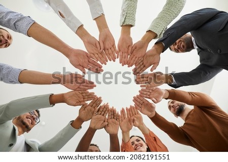 Group of happy diverse people joining hands. Mixed race team of different smiling young people putting hands together, cropped shot from below. Teamwork, community, help, support, volunteering concept Royalty-Free Stock Photo #2082191551