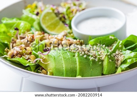 Green detox salad with avocado, sprouts, hemp seeds and yogurt dressing, white tile background, close-up. Royalty-Free Stock Photo #2082203914
