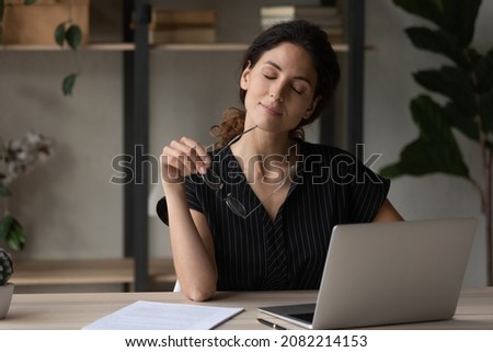 Putting job on pause. Calm latina woman relax at desk take break from computer work hold eyewear in hand give rest to tired eyes. Young lady employee sit on workplace with closed eyes take glasses off Royalty-Free Stock Photo #2082214153
