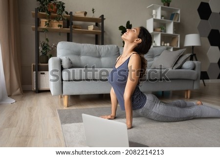 Strengthening muscles. Fit young hispanic woman do yoga exercises on floor before computer screen. Attractive millennial female practice cobra pose stretch shoulders and back reduce stress breath deep Royalty-Free Stock Photo #2082214213