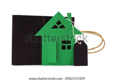 Property concept with cut out paper home and blank label tag near black paper shopping bag over a white background