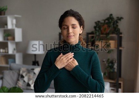 Blissful minute. Peaceful young latin female stand alone keep eyes closed put hands on heart pray thank god for kind wonderful things in life. Sincere lady feel grateful to fate for every good moment Royalty-Free Stock Photo #2082214465