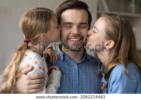 Joyful cute little kid daughter and loving young mother kissing handsome sincere father, showing affectionate feeling at home, friendly multigenerational family expressing devotion, relations concept.