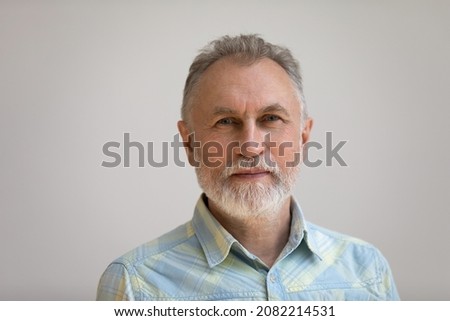 Serious older man in casual with beard head shot portrait. Grey haired retiree, pensioner posing, standing isolated against white wall background. Close up male portrait, elderly age concept