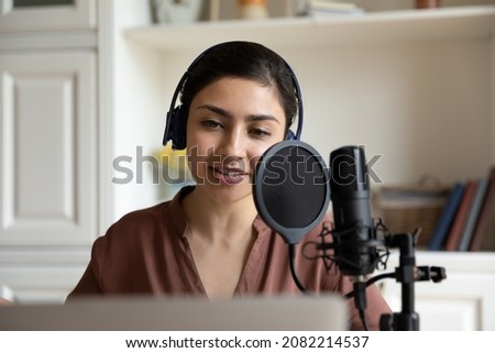 Head shot beautiful young indian ethnicity woman in headphones talking in professional stand microphone, recording audio for personal blog, singing song or voice acting using computer applications. Royalty-Free Stock Photo #2082214537