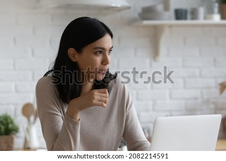 Young 25s thoughtful Asian woman sit indoor with laptop, thinks over task, makes telecommute job, deep in thoughts looks into distance. Modern tech, challenge, search solution and inspiration concept Royalty-Free Stock Photo #2082214591