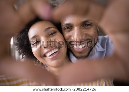 Happy young Black couple faces in finger heart shaped frame. Close up portrait. Millennial man and woman in love, having fun, posing, looking at camera, smiling, enjoying being together