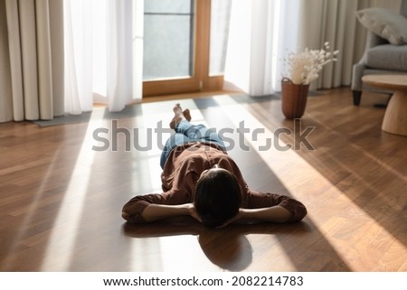 Relaxed happy young indian ethnicity woman homeowner lying alone on warm wooden floor with underfloor heating, enjoying carefree peaceful weekend leisure time alone in modern stylish living room. Royalty-Free Stock Photo #2082214783