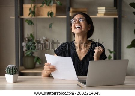 That is famous. Euphoric latina female office employee read official notification of promotion career salary growth. Excited young lady laugh celebrate business success holding paper financial report Royalty-Free Stock Photo #2082214849