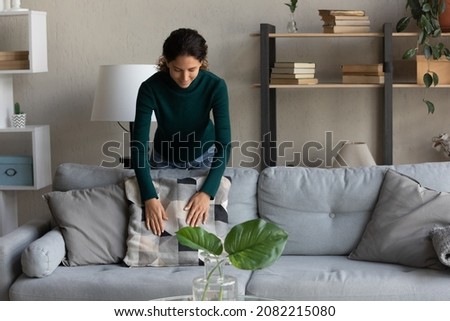 My sweet homey. Happy millennial latin woman homeowner arranging pillows on comfortable sofa with love care. Young hispanic lady decorating living room area in modern designed flat doing housekeeping Royalty-Free Stock Photo #2082215080
