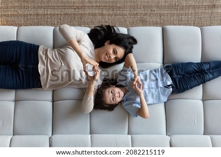 Above view happy Asian mom and little cute Caucasian son lying on couch smile looking at camera making heart shape with fingers showing symbol of love. Adoption, custody, cherish, family bond concept Royalty-Free Stock Photo #2082215119