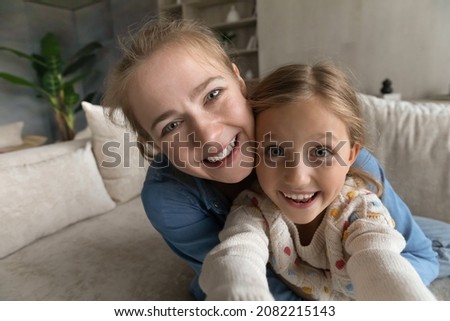 Close up sincere adorable little child girl having fun with happy loving mother, recording funny video or vlogging streaming stories online in social networks, posing for selfie photo, web camera view