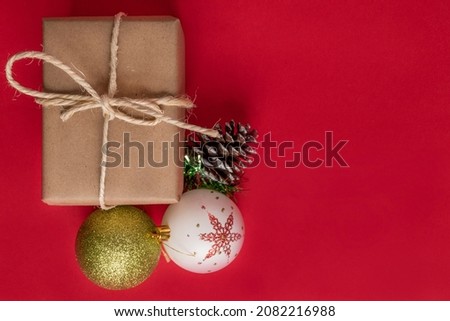 pink background with a gift box wrapped in paper with a cord bow next to Christmas balls to decorate, objects in studio, holiday
