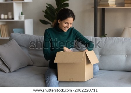 Ecommerce. Satisfied young latin woman web shop customer sit on sofa open postal delivery package with consumer goods products ordered online. Happy millennial lady unpacking after moving to new home Royalty-Free Stock Photo #2082220711