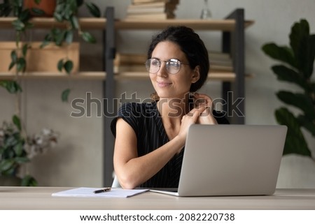 Optimistic dream. Smiling latina female employee sit at workplace distracted from office laptop screen relax visualize future career growth. Young woman enterpreneur thinking on good business decision