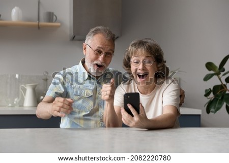 Excited happy elder couple getting awesome message with good surprising news, looking at smartphone screen, shouting for joy, making winner gesture, celebrating win, achieve, success, luck Royalty-Free Stock Photo #2082220780