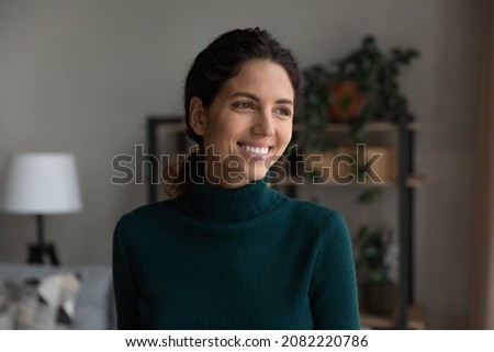 Beautiful smile. Head shot of smiling carefree hispanic female standing at living room looking aside lost in positive optimistic thoughts. Happy young lady enjoying life dreaming visualizing at home Royalty-Free Stock Photo #2082220786