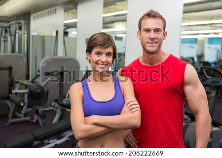 Fit attractive couple smiling at camera at the gym