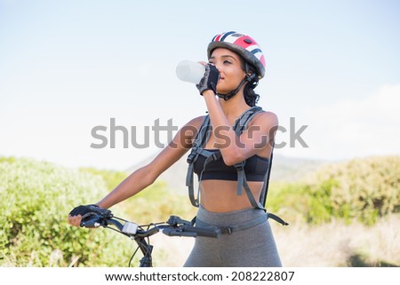 Fit woman going for bike ride drinking water on a sunny day in the countryside