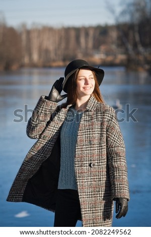 Spring photo of a girl in a hat and a gray coat against the background of melting snow.
