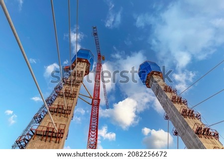 Construction of a new road bridge. Cable-stayed bridge, cables, towers, cargo crane. Construction site background with blue sky and clouds. Picture for the desktop. 