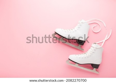 White female figure skates on light pink table background. Pastel color. Sport accessories for activities. Closeup. Empty place for text.