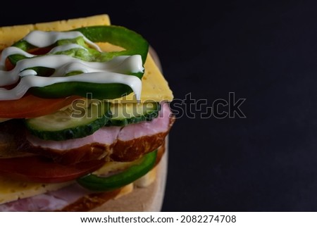 Close-up photo of a club sandwich. Sandwich with meat, ham, peppers, vegetables, tomatoes, onions and sauce on fresh sliced ​​rye bread on a wooden background.