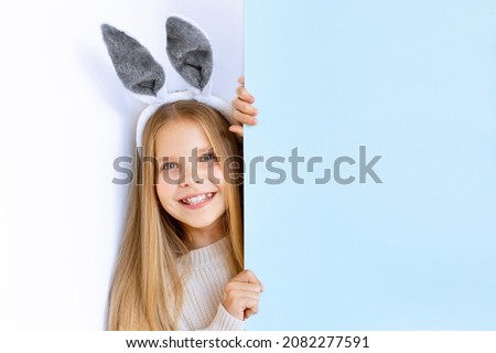 baby girl with rabbit ears, smiling and looking behind a blue background, easter, banner