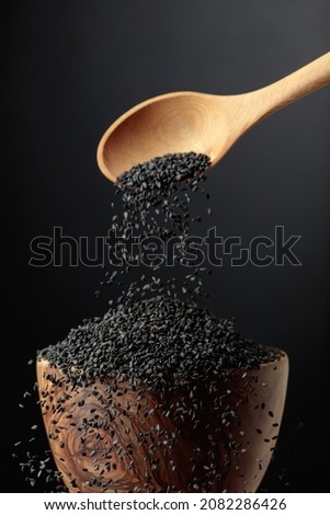 Grains of black sesame are poured with a wooden spoon in the bowl. Black sesame on a dark background. Copy space. Royalty-Free Stock Photo #2082286426