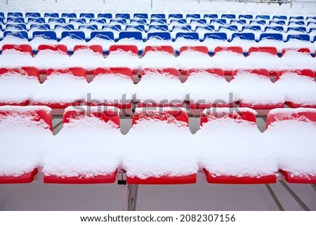 Stadium seats under the snow, red and blue chairs under the snow in winter