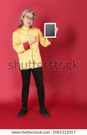 The senior Asian man wearing traditional gold chinese dresses standing on the red background.